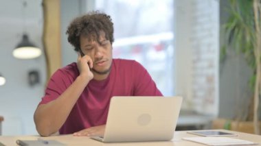 Young African Man Talking on Phone while using Laptop