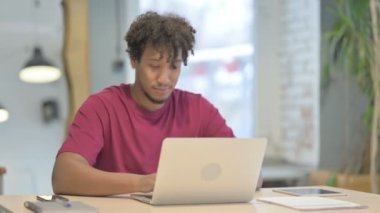 Young African Man Pointing at Camera while using Laptop