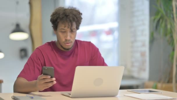 Young African Man Using Smartphone While Using Laptop — Vídeos de Stock