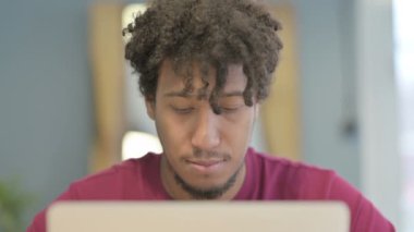 Close Up of Young African Man Smiling at Camera while using Laptop