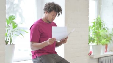 Young African Man Reading Documents while Sitting in Window