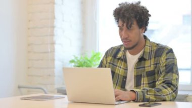 Young African Man Celebrating Online Success on Laptop in Office
