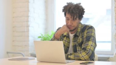 Pensive Young African Man Thinking while Working on Laptop