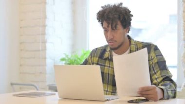 Young African Man Working on Laptop and Documents