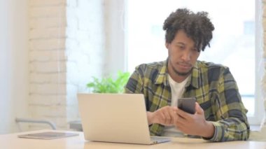 Young African Man using Smartphone while using Laptop