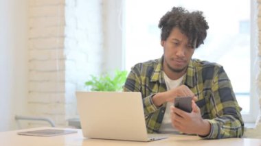 Young African Man Browsing Smartphone while Sitting in Office