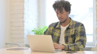 Young African Man Pointing at Camera while using Laptop