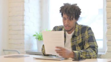 Young African Man Reading Documents in Office, Doing Paperwork