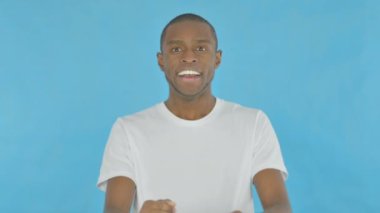 Successful Young African Man Celebrating Achievement on Blue Background