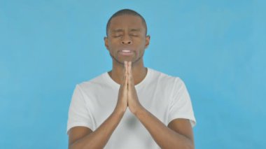 Young African Man Praying to God on Blue Background