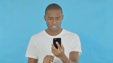 Young African Man Celebrating on Smartphone on Blue Background