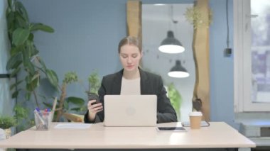 Young Businesswoman using Smartphone while using Laptop