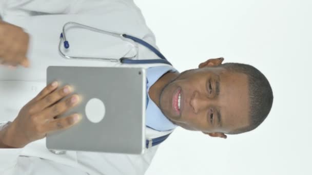白の背景に若いアフリカの医師によるタブレット上でのビデオ通話の垂直ビデオ — ストック動画