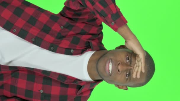 緑の背景を見回す若いアフリカ人男性の垂直ビデオ — ストック動画