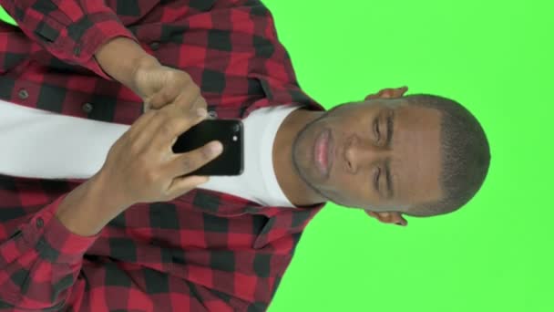 緑の背景にスマートフォンで損失を持つ若いアフリカ人男性の垂直ビデオ — ストック動画