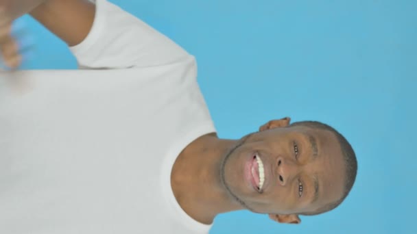 青の背景に手を振って若いアフリカ人男性の垂直ビデオ — ストック動画