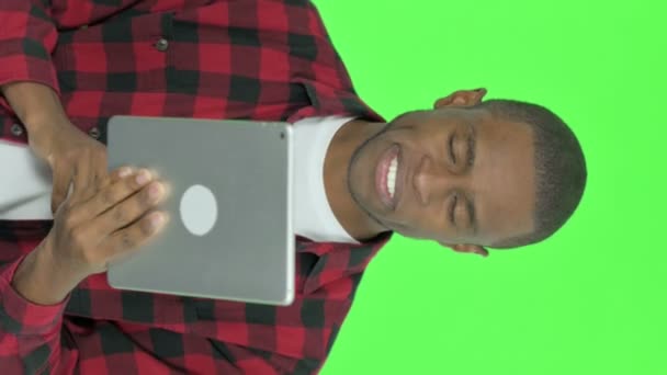 緑の背景に若いアフリカ人男性によるタブレット上でのビデオ通話の垂直ビデオ — ストック動画