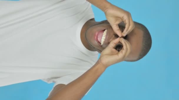 青い背景に手作り双眼鏡で若いアフリカ人男性を検索する垂直ビデオ — ストック動画