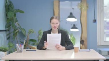 Young Businesswoman Celebrating Success while Reading Documents in Office