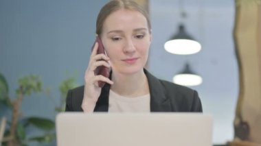 Close Up of Young Businesswoman Talking on Phone while using Laptop