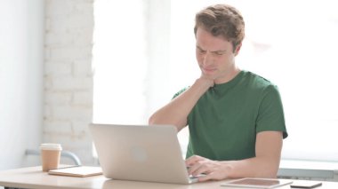 Dizüstü bilgisayar kullanırken boyun ağrısı çeken sıradan bir genç adam.