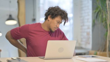 Genç Afrikalı Adam dizüstü bilgisayar kullanırken sırt ağrısı çekiyor
