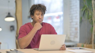 Young African Man Thinking while Working on Laptop