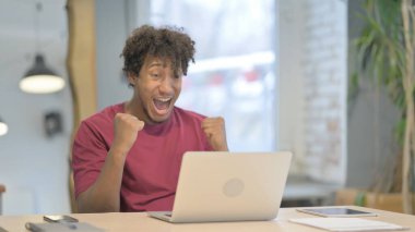 Young African Man Celebrating Online Success on Laptop in Office