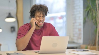 Displeased Young African Man Talking Angrily on Smartphone at Work