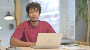 Dizüstü bilgisayar kullanırken kameraya bakan genç Afrikalı adam