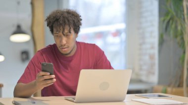 Young African Man using Smartphone while using Laptop