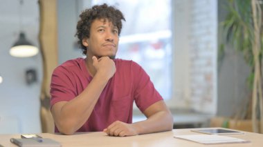 Pensive Young African Man Thinking while Sitting at Work