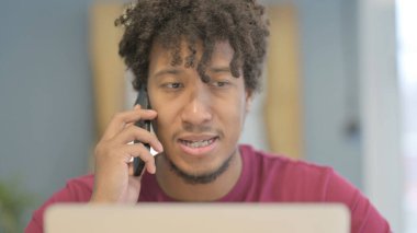 Close Up of Young African Man Talking on Phone while using Laptop