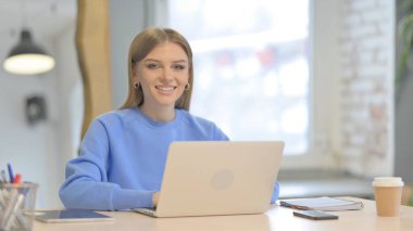 Dizüstü bilgisayar kullanırken Kameraya Gülümseyen Genç Kadın
