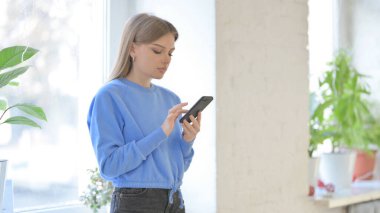 Young Woman using Smartphone while Sitting in Window