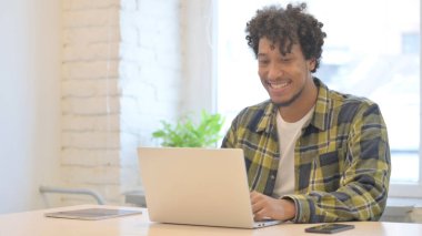 Young African Man Cheering Results on Laptop in Office