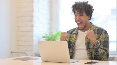 Young African Man Celebrating Online Success on Laptop in Office
