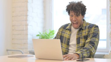 Shocked Young African Man Celebrating Win on Laptop in Office