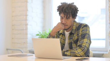Pensive Young African Man Thinking while Working on Laptop