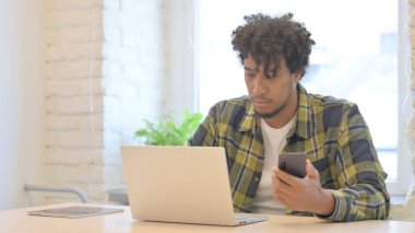 Young African Man using Smartphone while using Laptop