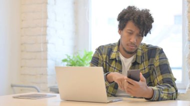 Young African Man Browsing Smartphone while Sitting in Office