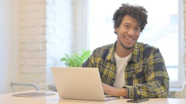 Dizüstü bilgisayar kullanırken kameraya gülümseyen genç Afrikalı adam