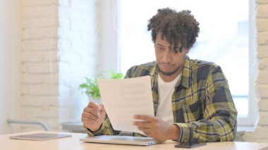 Young African Man Reading Documents in Office, Doing Paperwork