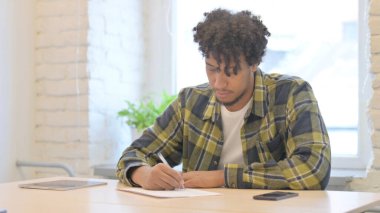 Young African Man Writing Letter in Office