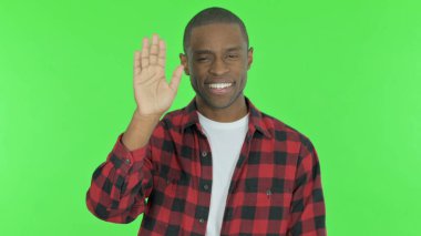 Young African Man Waving Hand to Say Hello on Green Background