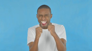 Successful Young African Man Celebrating Achievement on Blue Background