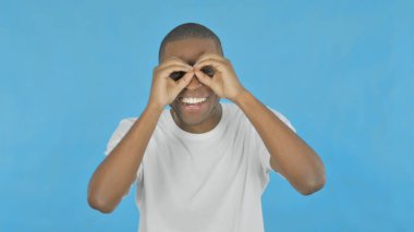 Excited Young African Man Searching with Handmade Binocular on Blue Background