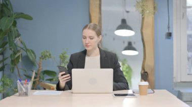 Young Businesswoman using Smartphone while using Laptop