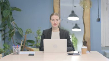 Young Businesswoman Looking at Camera while using Laptop