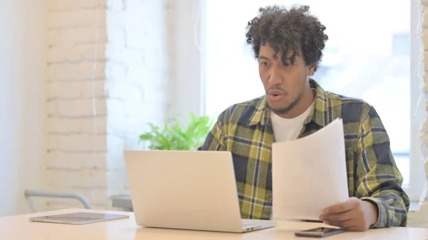 Young African Man Celebrating Success while Reading Documents in Office